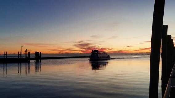 Eine Hafeneinfahrt, durch die ein Boot fährt. Der Himmel wird von der untergehenden Sonne angeleuchtet. © Monika Wagenfuehr Foto: Monika Wagenfuehr