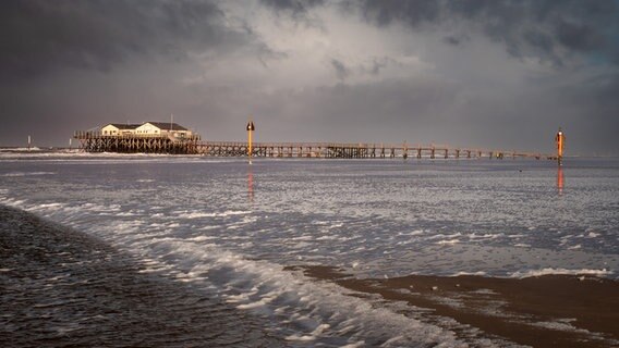 Ein von Wasser überspülter Sandstrand. Am Horizont eine der landestypischen Pfahlbauten. © Thorsten Klüver Foto: Thorsten Klüver