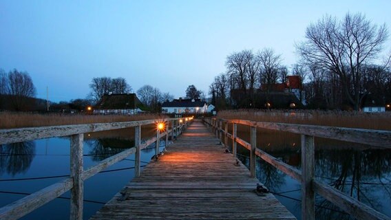 Eine Brücke führt zu einem Ufer, an dem sich mehrere Häuser befinden. © Heike Greggersen Foto: Heike Greggersen