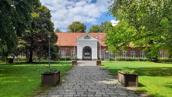 Ein Weg zwischen zwei Bäumen führt auf ein Rotes Backsteingebäude zu. © Marita Volkmann Foto: Marita Volkmann