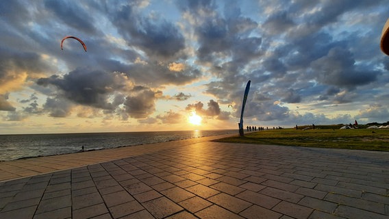 Die Sonne geht über der Nordsee unter während vor Büsum noch Kitesurfer unterwegs sind. © Elisabeth Weidel Foto: Elisabeth Weidel