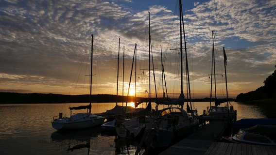 Segelboote liegen an einem Steg, am Horizont geht die Sonne unter. © Udo Lunddahl Foto: Udo Lunddahl