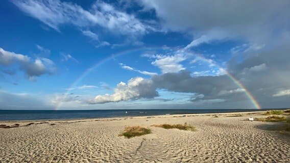 Ein Regenbogen am Strand: Er strahlt über den Horizont am strahlenden Himmel. Der Sand scheint im Sonnenlicht. © Yorck Koch Foto: Yorck Koch