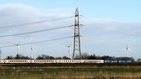 Die Bahn fährt in Risum-Lindholm an Windrädern und einem Strommast vorbei. © Cordula Sönnichsen Foto: Cordula Sönnichsen