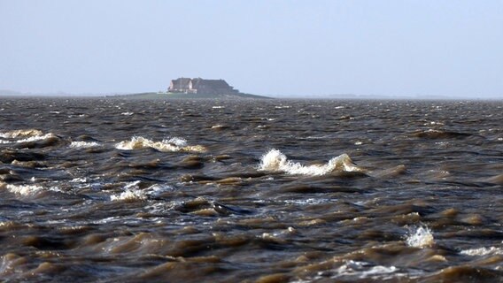 Wellengang auf der Nordsee, am Horizont ist ein Haus auf einer Insel zu sehen. © Wally Bumann Foto: Wally Bumann