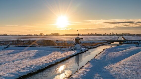 Die Sonne geht über einer Mühle im verschneiten Marschland auf. © Thomas Neuss Foto: Thomas Neuss