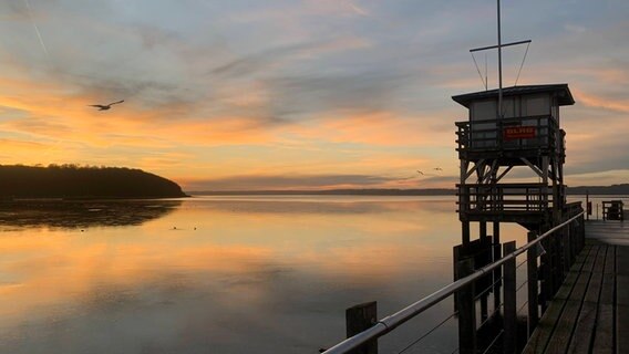 Sonnenuntergang an einem Anleger, im Vordergrund steht ein Turm der DLRG. © Hans Christian Lorenzen Foto: Hans Christian Lorenzen