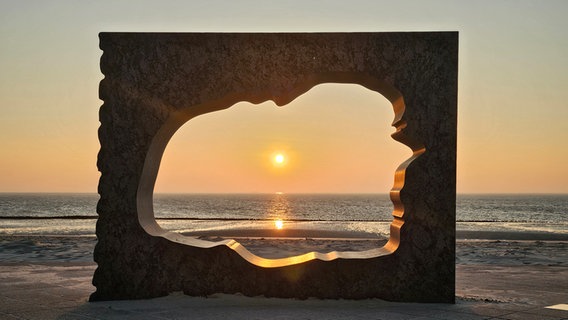 Die aufgehende Sonne scheint durch eine Statur am Strand von Wyk. © Hannes Kiessling Foto: Hannes Kiessling