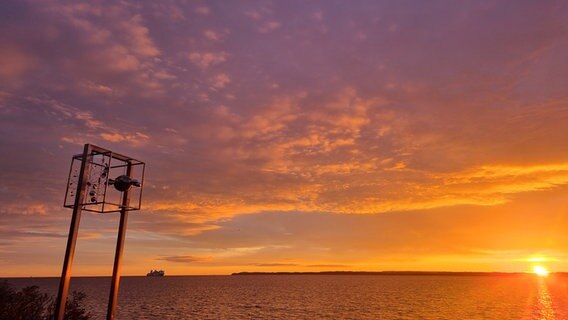 Ein Windspiel vor dem Wasser bei Sonnenuntergang. In der Ferne ist ein Schiff zu sehen. © Henning Dierken Foto: Henning Dierken
