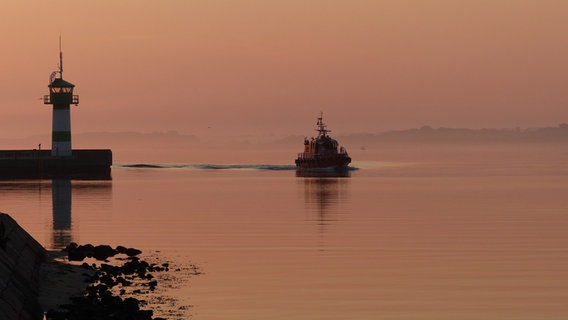 Ein Lotsenschiff bei der Einfahrt in die Trave vorbei am Leuchtturm zum Sonnenaufgang in Travemünde © Sandra Polzin Foto: Sandra Polzin