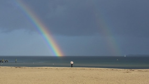 Eine Person steht am Strand von Travemünde und betrachtet einen Regenbogen. © Beate Männel Foto: Beate Männel