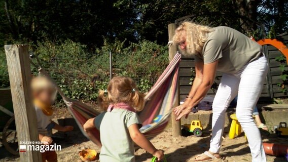 Eine Frau spielt mit einigen Kindern auf einem kleinen Spielplatz. © NDR Foto: NDR Screenshots