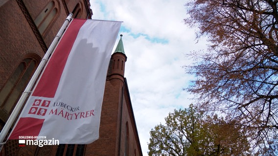 Eine Fahne weht auf einem Museum in Lübeck, auf dieser sind die "Lübecker Märtyrer" abgebildet. © NDR Foto: NDR Screenshots
