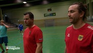 Zwei Handballspieler stehen auf dem Spielfeld und hören den Instruktionen des Trainers zu. © NDR Foto: NDR Screenshots