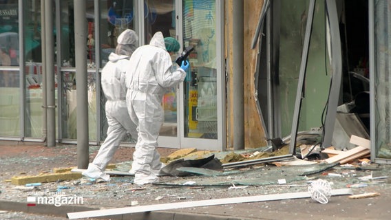 Zwei Personen in Schutzanzügen stehen vor den Trümmern des Geldautomaten. © NDR 