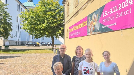 Eine Gruppe von Menschen steht nehmen einem Banner, dass auf eine Ausstellung auf Schloss Gottorf 1.5 - 3.11.2024 hinweist. © Schloss Gottorf Foto: Frank Zarp