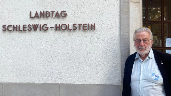 Flüchtlingsbeauftragter Stefan Schmidt steht vor dem Eingang zum Landtag Schleswig-Holstein neben dem gleichnamigen Schild an der Wand. © NDR Foto: Anna Grusnick