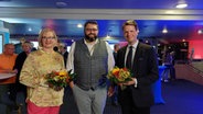 Die Oberbürgermeisterwahl-Kandidaten von Norderstedt, Katrin Schmiederer und Robert Hille haten einen Blumenstrauß in der Hand und lächeln. In der Mitte steht der Wahlleiter von Norderstedt. © Stadt Norderstedt 