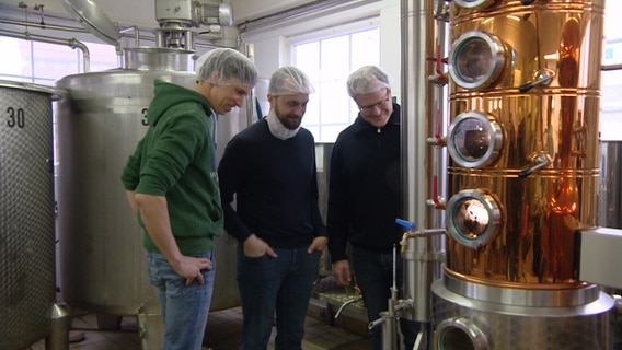 Drei Männer blicken auf eine Destille.  