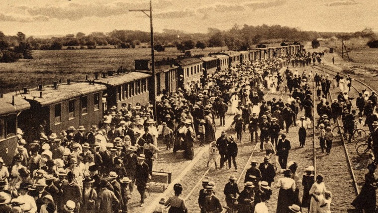 Ein historisches Bild zeigt Hunderte Menschen am Bahnhof Schönberger Strand, datiert mit "um 1912" © Projekt Spurensuche