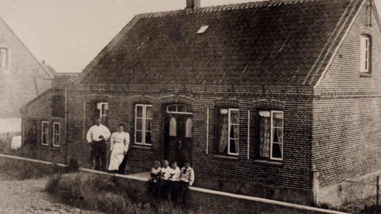 Das historische Bild zeigt das Haus von Wilhelm Linnig, er steht mit Frau Ella davor, die Kinder sitzen auf einem Wall am Weg, der das Grundstück abgrenzt. © Projekt Spurensuche