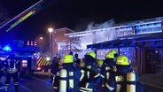 Einsatzkräfte der Feuerwehr vor einem Gebäude aus dessen Fenstern Rauch quillt. Es ist dunkel. © telenewsnetwork (TNN) 