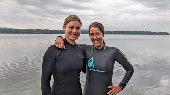Die Schwimmerinnen Maxi Bierewirtz und Franziska Sieber stehen in Neoprenanzügen Arm in Arm vor dem Ratzeburger See. © Ellinor Skogland 