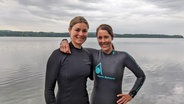Die Schwimmerinnen Maxi Bierewirtz und Franziska Sieber stehen in Neoprenanzügen Arm in Arm vor dem Ratzeburger See. © Ellinor Skogland 