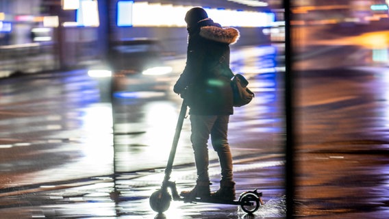 Ein Mensch fährt in der Dunkelheit mit einem E-Scooter über eine beleuchtete Straße. © picture alliance / Jochen Tack | Jochen Tack Foto: Jochen Tack