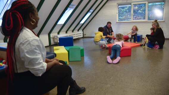 Mehrere Kinder spielen unter Aufsicht von drei Erwachsenen in einem Raum. © NDR 