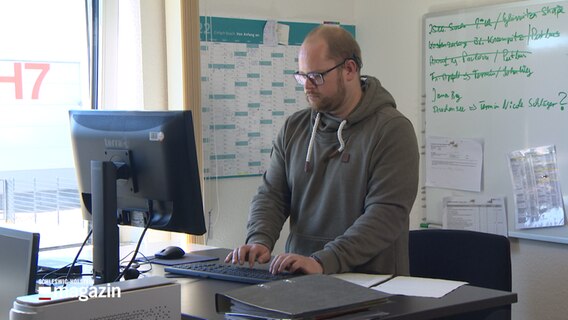 Ein Mann steht an einem Schreibtisch und arbeitet an einem Computer. © NDR 