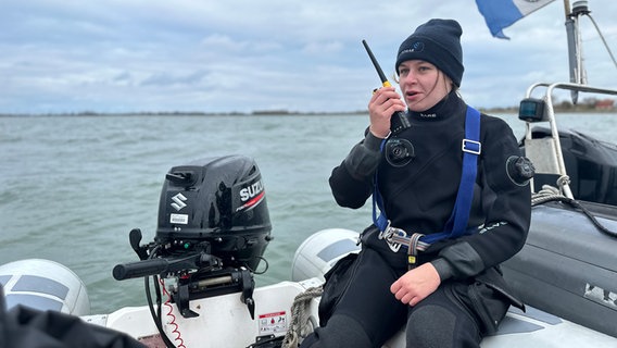 Eine Frau spricht, auf einem Boot sitzend, in ein Funkgerät. © NDR Foto: Jörn Zahlmann