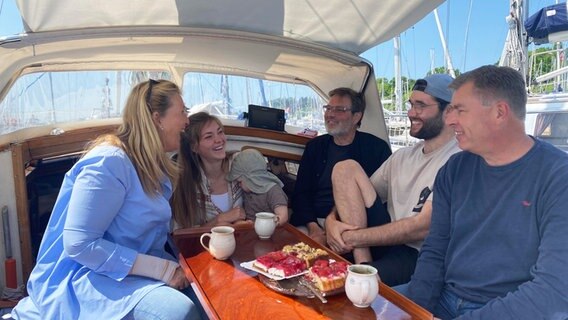 Sechs Personen sitzen bei Kaffee und Kuchen auf einem Segelboot © NDR Foto: Andrea Schmidt