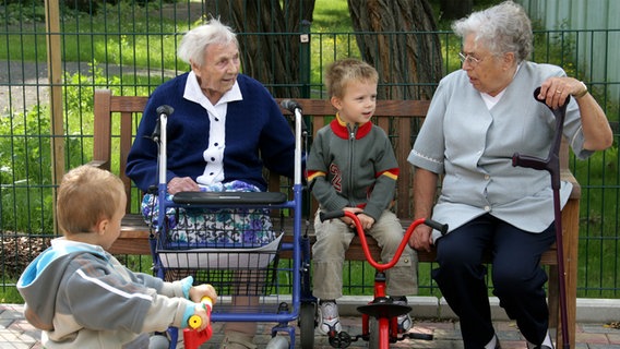 Zwei Seniorinnen sitzen mit zusammen mit zwei Kindern auf einer Bank. © picture alliance / ZB Foto: Waltraud Grubitzsch