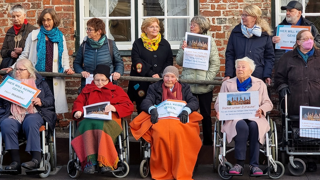 Bewohner sitzen in Rollstühlen vor dem Heiligen-Geist-Hospital, eingepackt in dicke Decken, halten Plakate hoch. Etwa 80 Senioren und Angehörige demonstrieren.