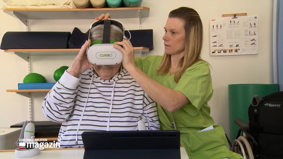 Eine Patientin bekommt von einer Physiotherapeutin eine VR-Brille aufgesetzt © NDR 