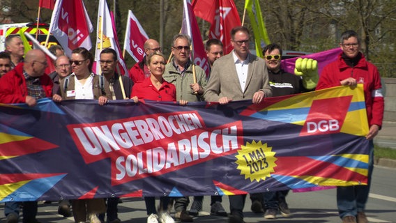 Menschen laufen bei einer Mai-Kundgebung mit einem Banner mit der Aufschrift "Ungebrochen solidarisch" durch Lübeck © NDR 