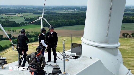 Der Bundespräsident Frank-Walter Steinmeier steht, gesichert durch Kletterausrüstung und Helm, auf einem Windrad in 130 Meter Höhe. © NDR Foto: NDR Screenshots