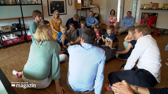 Kinder und Erwachsene sitzen in einer KiTa auf dem Boden. Unter ihnen ist auch Schleswig-Holsteins Ministerpräsident, Daniel Günther. © NDR Foto: NDR Screenshots