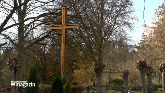 Friedhof im Herbst großes Kreuz inmitten von Grabsteinen © NDR Foto: NDR Screenshot