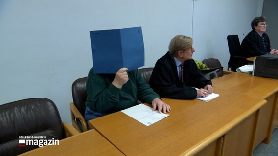 Ein wegen Kindesmissbrauch in Angeklagter sitzt in einem Gerichtssaal und verdeckt sein Gesicht mit einer Mappe. © NDR Foto: NDR Screenshot
