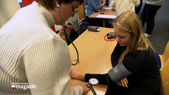 Eine Frau misst den Blutdruck bei einer Schülerin. © NDR Foto: NDR Screenshot