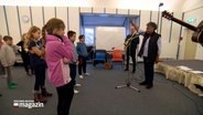 Eine Frau leitet eine Gruppe von Schülern bei einer Gesangsstunde zu Gospelmusik. © NDR Foto: NDR Screenshot