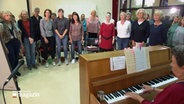Im Halbkreis stehen Frauen um ein Klavier und singen, eine Probe des Lübecker Popchors. © NDR Foto: NDR Screenshot