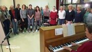 Im Halbkreis stehen Frauen um ein Klavier und singen, eine Probe des Lübecker Popchors. © NDR Foto: NDR Screenshot