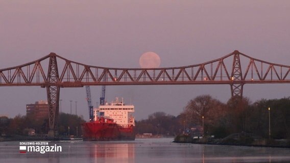 Ein Schiff fährt unter einer Brücke hindurch, über der Brücke ist der Mond am Himmel © NDR Foto: NDR Screenshot