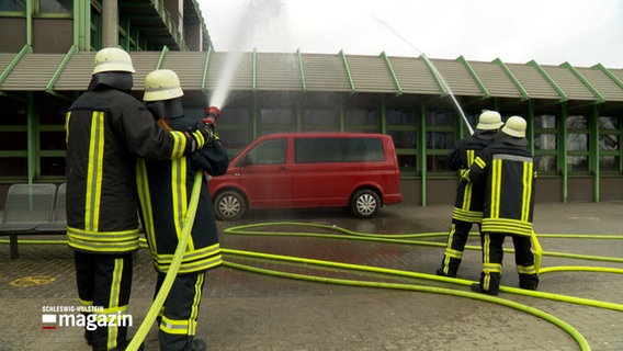 Vier Feuerwehrleute löschen bei einer Übung einen Kleinbus. © NDR Foto: NDR Screenshot