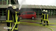 Vier Feuerwehrleute löschen bei einer Übung einen Kleinbus. © NDR Foto: NDR Screenshot