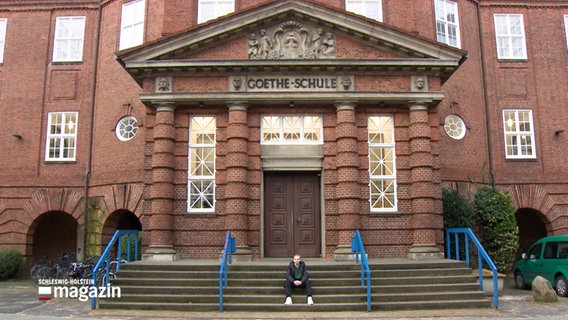 Vor dem Portal der Goetheschule in Flensburg sitzt ein einzelener Schüler auf der Treppe © NDR Foto: NDR Screenshot