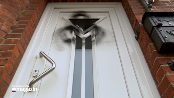 Auf einer weißen Tür wurde mit schwarzer Farbe ein Grafitto gemalt © NDR Foto: NDR Screenshot